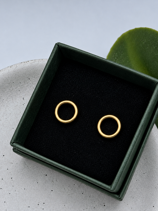 Gold circle stud earrings with a smooth rounded finish, handcrafted by Wild One Jewellery and photographed on a pale speckled ceramic dish.