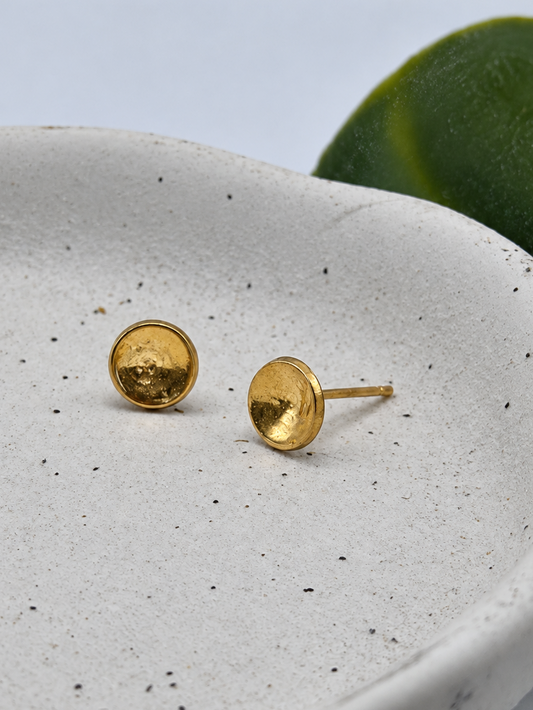 9ct gold New Moon stud earrings with a softly hammered, textured finish and reflective golden surface, photographed on a pale speckled ceramic dish by Wild One Jewellery.