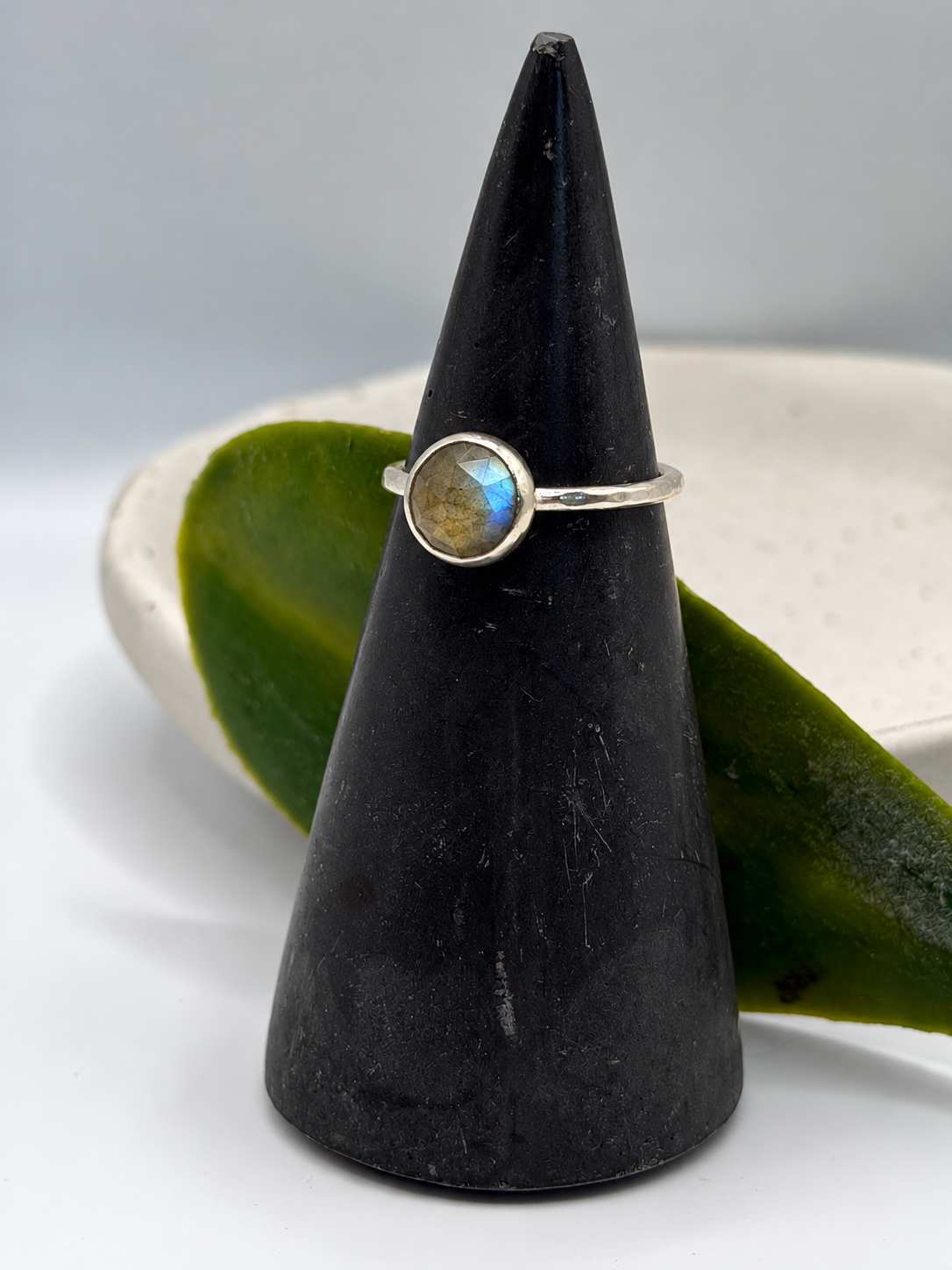 Handcrafted recycled sterling silver labradorite ring with a round faceted gemstone showing blue and golden flashes, displayed on a speckled ceramic dish.