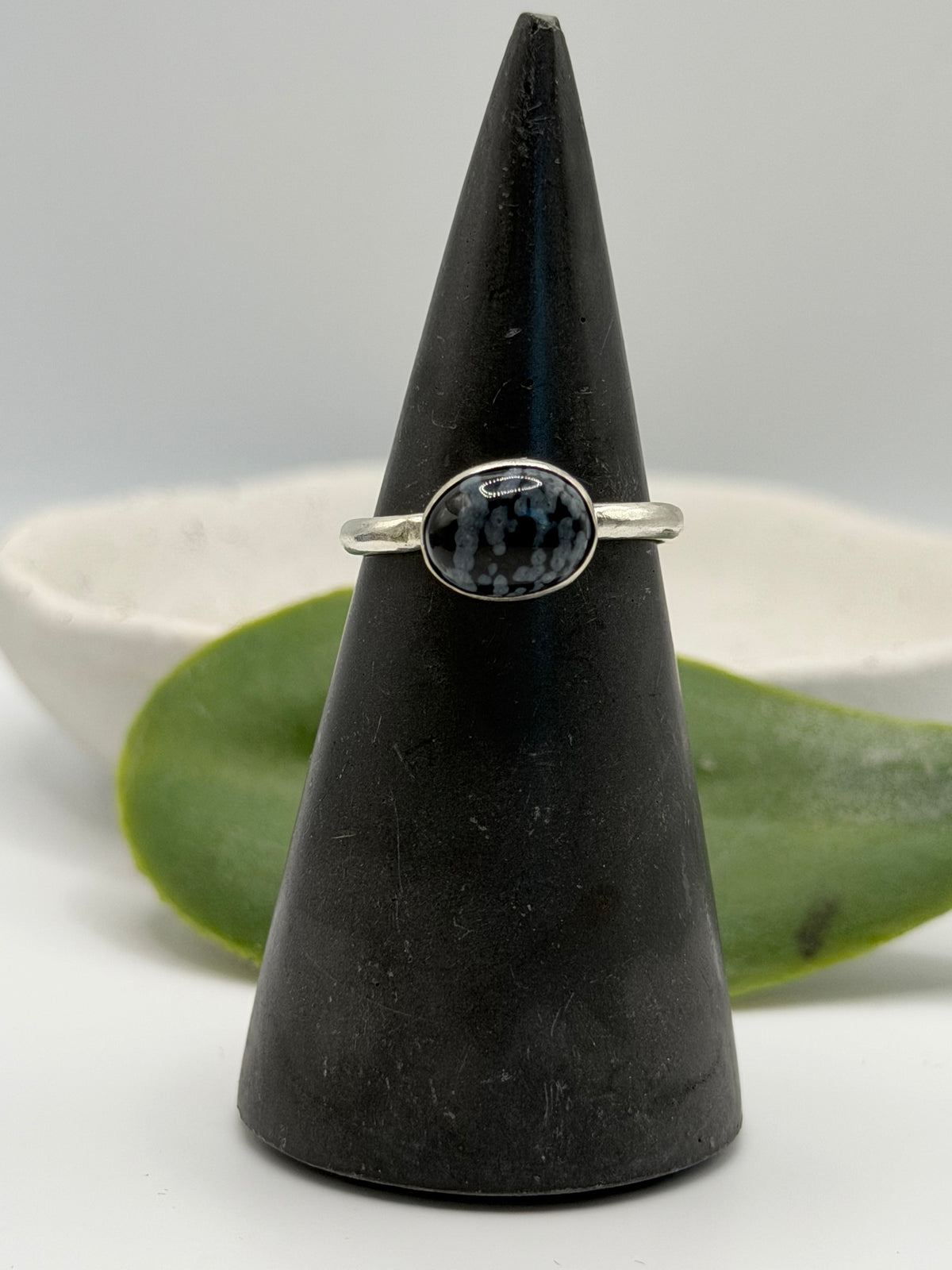 One-of-a-kind mini faceted snowflake obsidian ring from the Stone + Silver collection by Wild One Jewellery, featuring an oval black gemstone with pale snowflake-like markings set on a textured sterling silver pebble band.