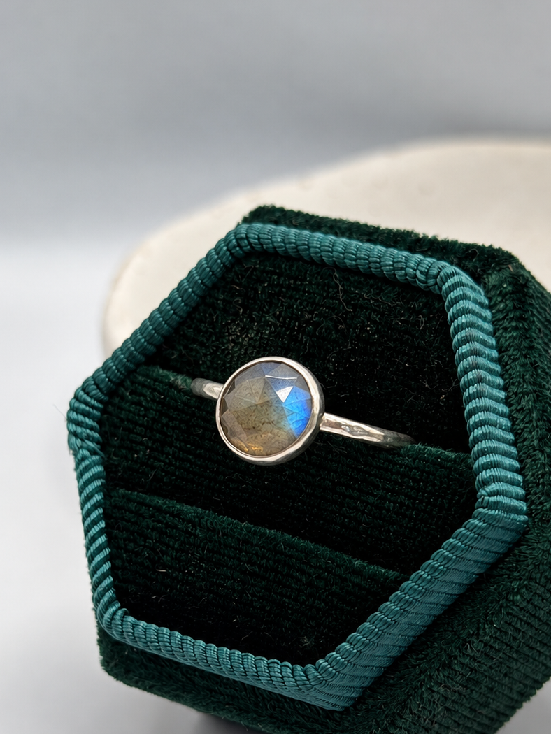 Handcrafted recycled sterling silver labradorite ring with a round faceted gemstone showing blue and golden flashes, displayed on a speckled ceramic dish.