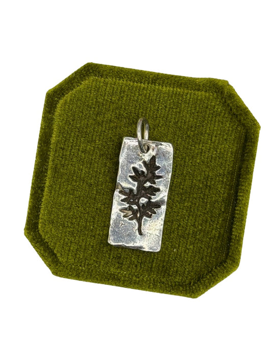 Handmade recycled sterling silver Midi Leaf charm with a dark botanical leaf imprint and textured rectangular pendant, displayed on an olive green velvet jewellery cushion by Wild One Jewellery.