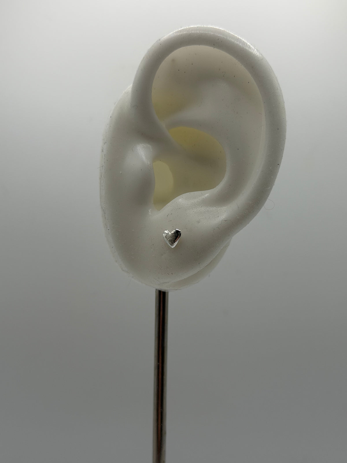 Minimal heart-shaped silver stud earrings with a reflective, textured finish, handmade in small batches.
