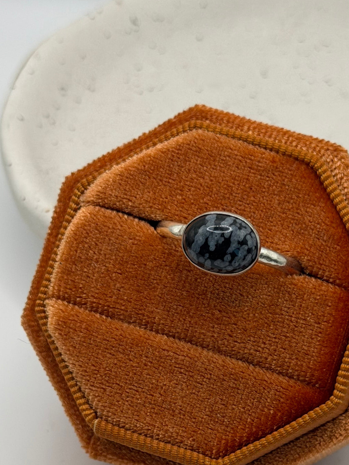 One-of-a-kind mini faceted snowflake obsidian ring from the Stone + Silver collection by Wild One Jewellery, featuring an oval black gemstone with pale snowflake-like markings set on a textured sterling silver pebble band.