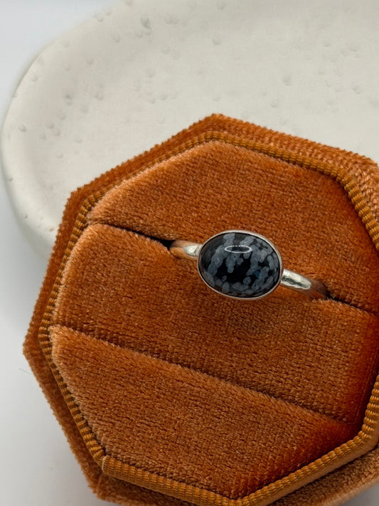 One-of-a-kind mini faceted snowflake obsidian ring from the Stone + Silver collection by Wild One Jewellery, featuring an oval black gemstone with pale snowflake-like markings set on a textured sterling silver pebble band.